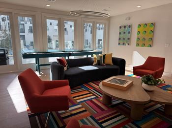 A living room with a black couch, a red chair, a wooden coffee table, and a colorful rug.